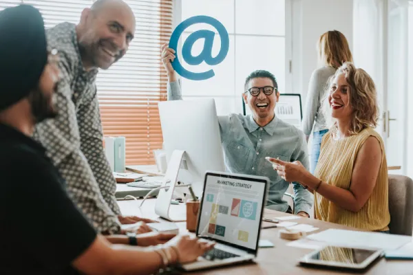 Diverse marketing team collaborating in a bright office with a laptop showing marketing strategy and an at-symbol icon.
