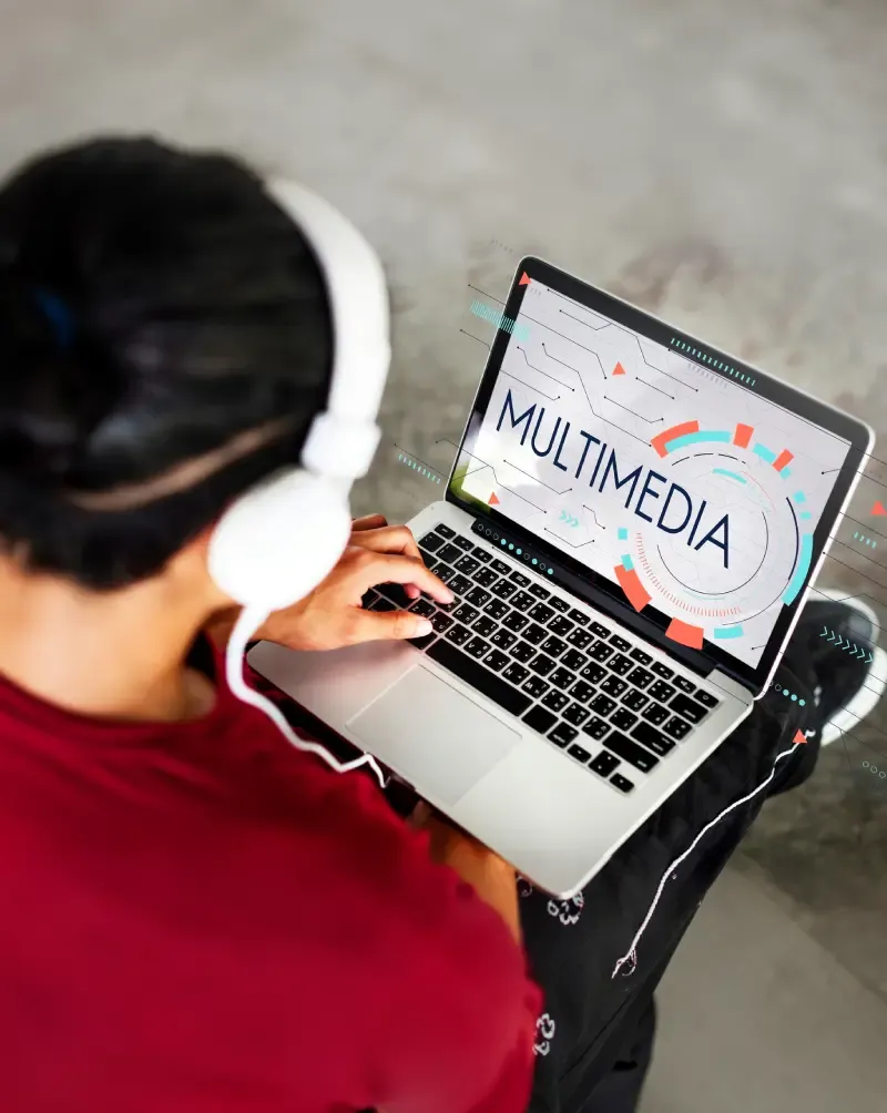 Person with headphones using a laptop showing a Multimedia graphic on screen.