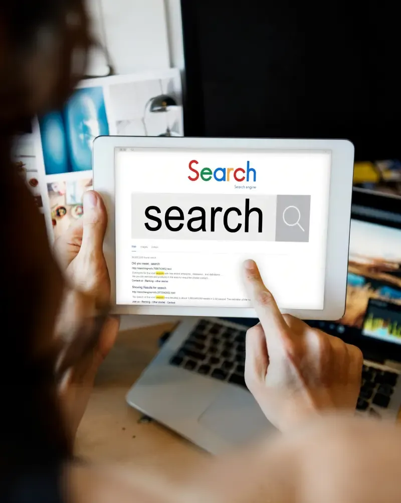 Hands holding a tablet showing a search engine results page with titles and snippets.