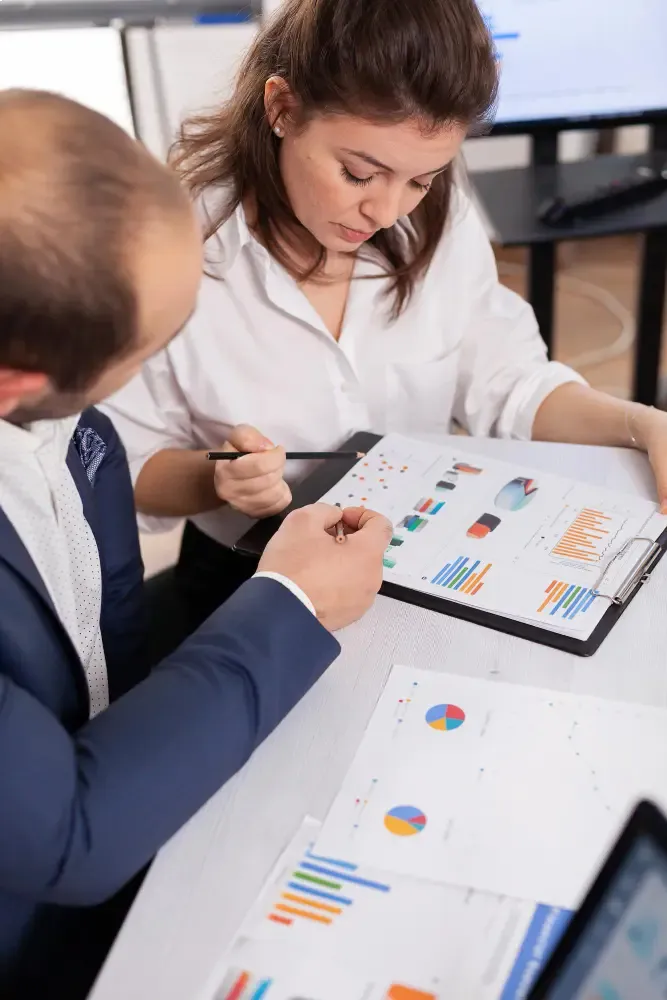 Two colleagues reviewing charts and performance printouts on a clipboard at a desk.