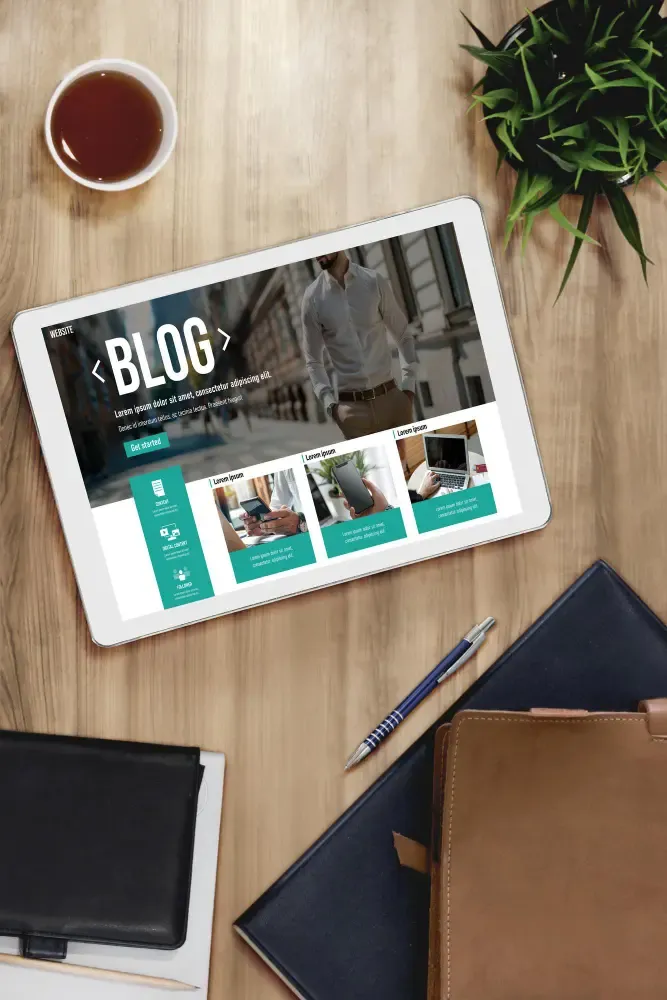 Tablet on a wooden desk showing a professional blog website layout, with coffee, a plant, and notebooks nearby.