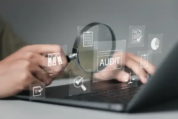 Hands on a laptop with a magnifying glass and floating AUDIT graphic—checklist, documents, and analytics icons—for discovery and content audit.